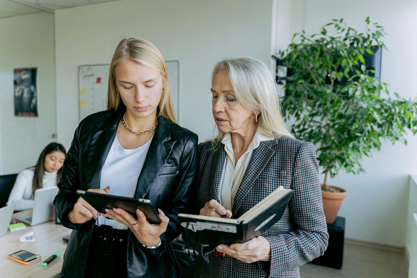 Professional women discussing work in a modern office setting with colleagues.